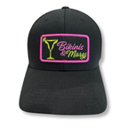 A black baseball cap with a rectangular embroidered patch on the front. The patch features a bright pink border, a green martini glass graphic, and the words 'Bikinis & Margs' in pink and green script.