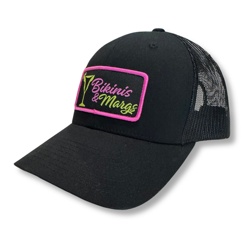 A black trucker-style cap with a curved brim, black mesh back, and a rectangular embroidered patch on the front reading 'Bikinis & Margs' in neon pink and green.