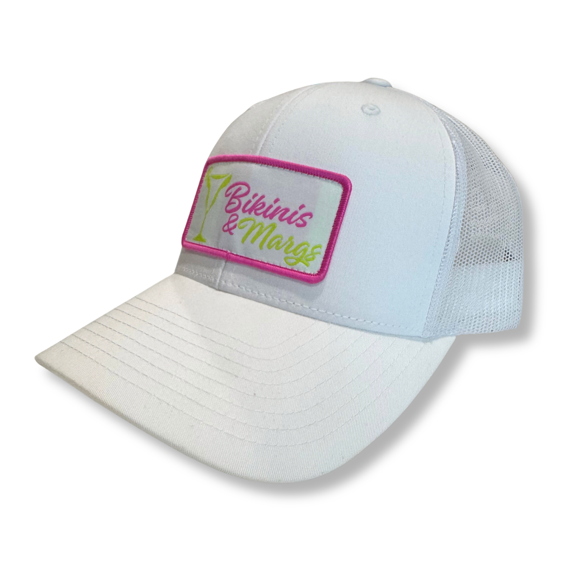 A white trucker-style baseball cap with a mesh back and a rectangular embroidered patch on the front. The patch has a pink border, a white background, and the text 'Bikinis & Margs' in pink and green script.